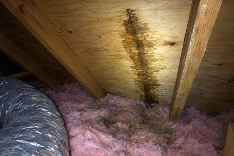 Underside of roof decking in an attic with a water trail running from a nail tip