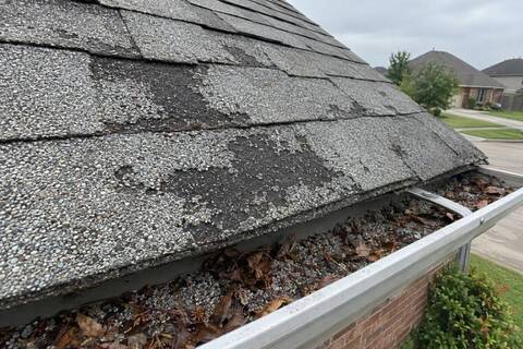 Aging shingle with worn granules and exposed mat beside loose granules