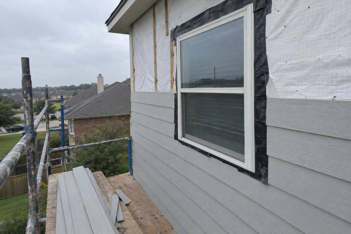 Fiber-cement lap plank being installed on a two-story wall with a level line and a flashed window head